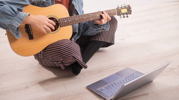 Young hipster woman sitting on the floor at home and watching guitar tutorials on laptop. Distance learning music in quarantine - Fotografie, Obrázek