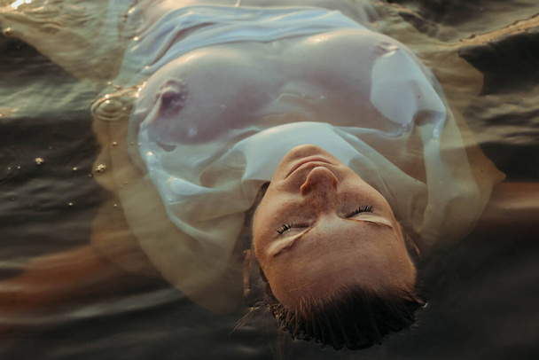 Porträt einer schönen jungen Frau im Wasser, mit Sommersprossen und grünen Augen. wunderschönes Sonnenuntergangslicht. athletische Körper, in der Nähe des Sees, vor dem Hintergrund des Wassers - Foto, Bild