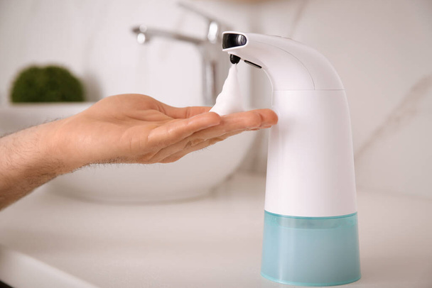 Man using automatic soap dispenser in bathroom, closeup - Fotó, kép