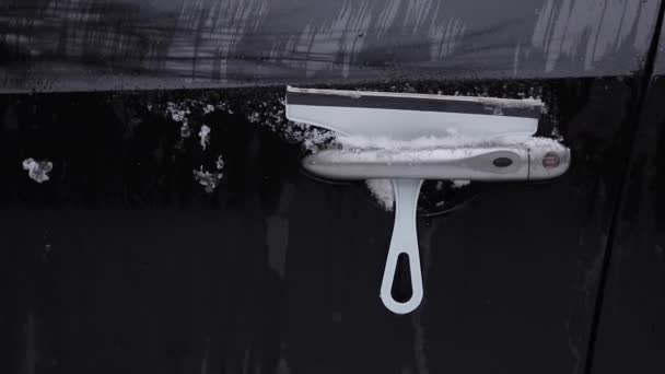 Κοντινό πλάνο του ανθρώπου καθαρίζει χιονισμένο παράθυρο σε ένα αυτοκίνητο με ξύστρα χιονιού. Συγκεντρώσου στον ξύστη. Κρύο χιονισμένο και παγωμένο πρωινό. Μαύρο αυτοκίνητο - Πλάνα, βίντεο
