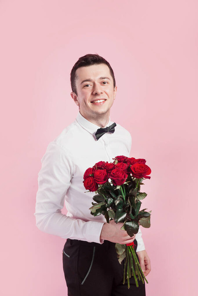 Valentines day. Handsome smiing boy holding flowers and gift box on pink background. - Fotó, kép
