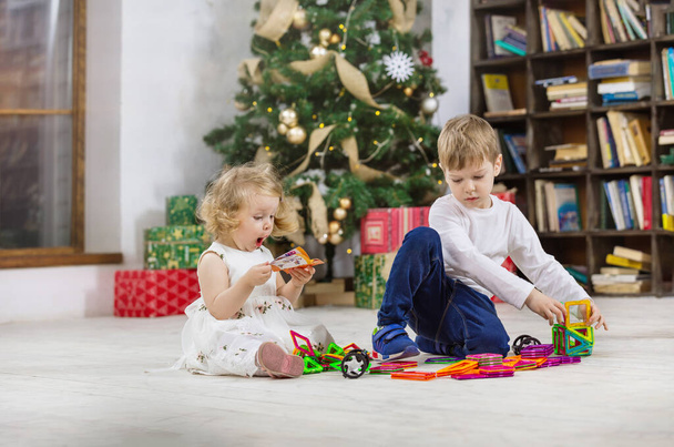 Junge und Mädchen spielen zu Hause mit Magnetspielzeug neben dem Weihnachtsbaum - Foto, Bild