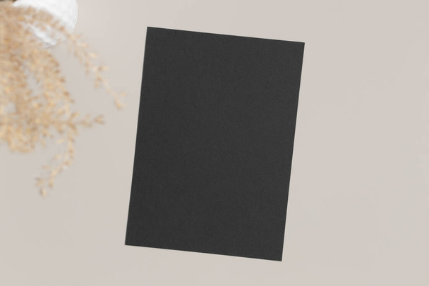 Чорна картка запрошення макет з висушеною травою на бежевому столі. 5x7 співвідношення, подібне до A6, A5
. - Фото, зображення