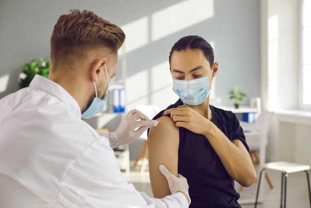 Fiatal férfi orvosi maszkban, szezonális influenza elleni oltással vagy modern Covid-19 vakcinával. - Fotó, kép