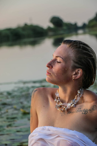 portrait of a beautiful young woman in the water, with freckles and green eyes. beautiful sunset light. athletic body, near the lake, against the background of water - Foto, afbeelding