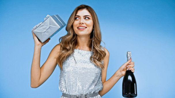 Mutlu kadın elinde hediye kutusu ve mavi kutuda izole edilmiş bir şişe şampanya tutuyor. - Fotoğraf, Görsel