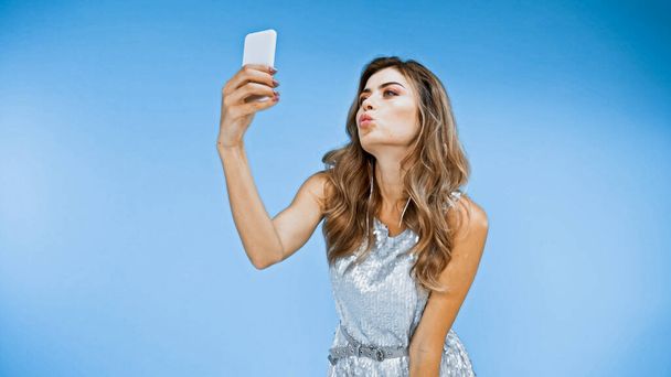donna che soffia bacio mentre prende selfie su blu - Foto, immagini