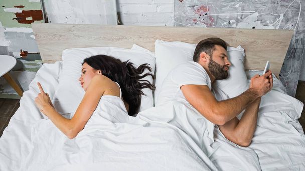 young couple messaging on smartphones while lying in bed back to back - Foto, Bild