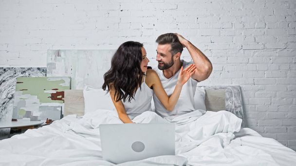 excited couple looking at each other while watching film on computer in bed - Zdjęcie, obraz
