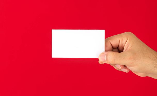 Kırmızı arkaplanda boş beyaz kartvizit gösteren bir adam - Fotoğraf, Görsel