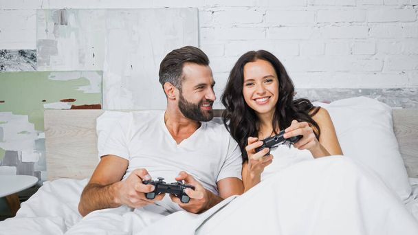 KYIV, UCRAINA - 26 GENNAIO 2021: coppia allegra che gioca ai videogiochi in camera da letto - Foto, immagini