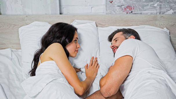 jeune homme et femme qui se regardent alors qu'ils sont couchés au lit - Photo, image