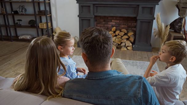 Children sitting near parents on blurred foreground on couch in living room  - Photo, Image