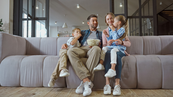 Smiling family with popcorn sitting on couch  - Photo, Image