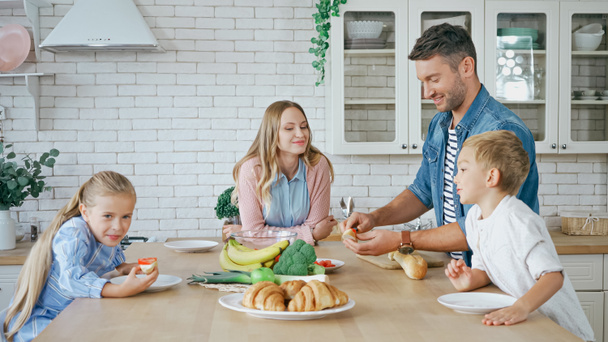 Vater hält Baguette neben Essen und Familie in Küche  - Foto, Bild