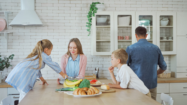 台所のテーブルの上に食べ物やペストリーの近くに立っている子供たちと家族  - 写真・画像