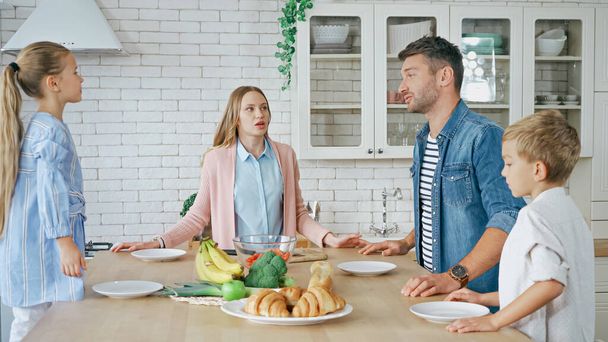 Rodzina z dziećmi rozmawia przy jedzeniu i talerzach na stole kuchennym  - Zdjęcie, obraz