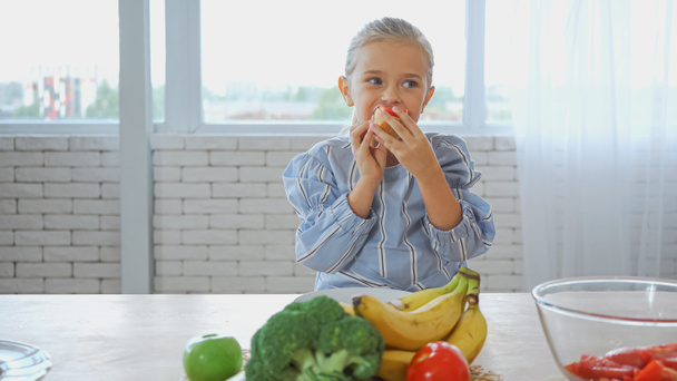 Chica comiendo baguette cerca de verduras frescas y frutas en primer plano borroso  - Foto, Imagen