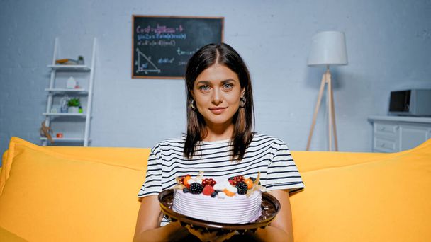 Young woman holding tasty cake on couch  - Valokuva, kuva