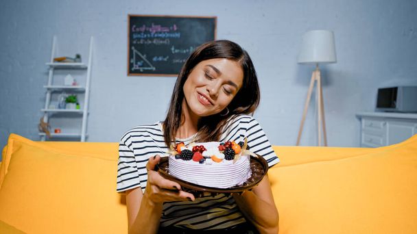 Smiling woman with closed eyes holding cake with cream and berries  - Photo, image