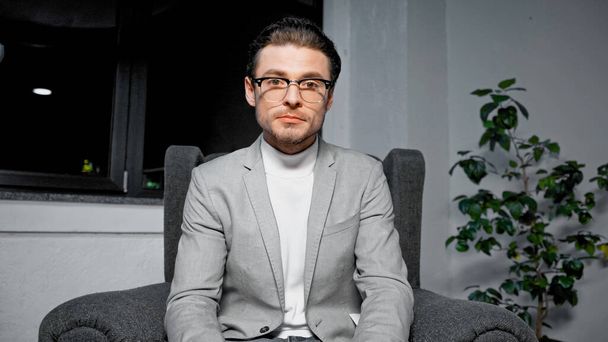 Young manager in eyeglasses looking at camera while sitting on armchair  - Foto, afbeelding