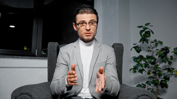 Young businessman in suit and eyeglasses talking at camera during video chat  - Foto, afbeelding