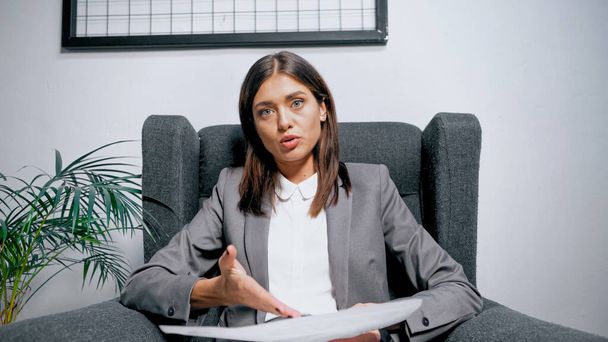 Mujer de negocios señalando el papel en primer plano borroso durante la videollamada en la oficina  - Foto, Imagen