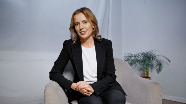 Smiling businesswoman in suit sitting on armchair in office  - Foto, immagini