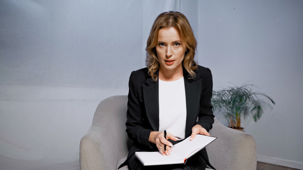 Adult businesswoman talking at camera and holding notebook and pen  - Foto, Imagem