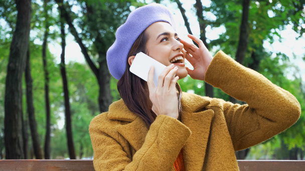 excited woman touching face and looking away while calling on mobile phone in park - Photo, Image