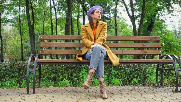 triste mujer mirando hacia otro lado mientras está sentado en el banco en el parque de otoño - Foto, imagen