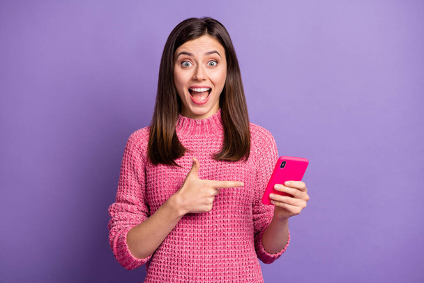 Photo portrait of amazed female brunette pointing finger cellphone staring opened mouth isolated on vivid purple color background - Foto, Imagem