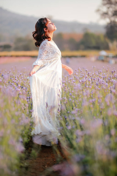 Blond long haired woman in lavender field. Style life enjoying journey to travel on vacation with relaxation with in long white dress outdoors on summer day. - Photo, Image