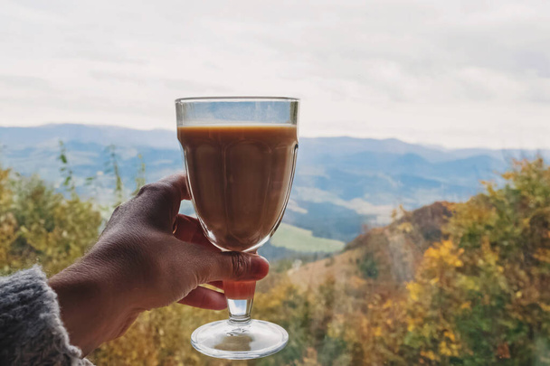 Woman holding a glass with chai latte with a view to mountains - Photo, image