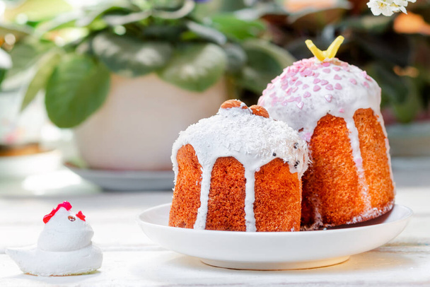 鶏の置物の横に皿の上に2つの装飾されたイースターケーキ。背景には、植物や花。イースター・フェスト. - 写真・画像