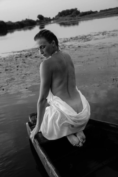 portrait of a beautiful young woman in the water, with freckles and green eyes nude, black and white photo. beautiful sunset light. athletic body, near the lake, against the background of water - Photo, Image