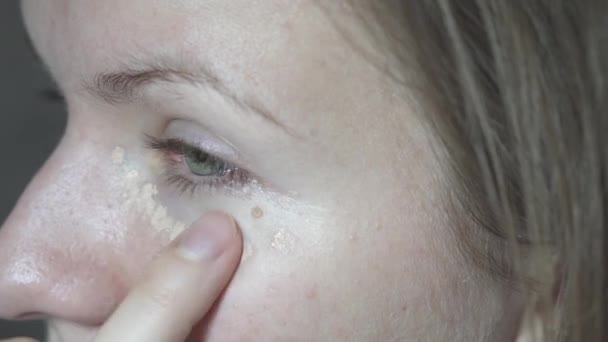 目の下の滑らかな顔の皮膚にシーラーを適用する若い女性。家にいて、近くにいて、 4k - 映像、動画