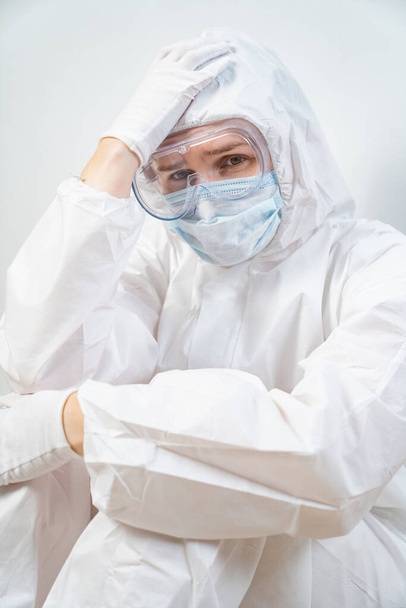 retrato de un médico cansado en traje protector, gafas, máscara contra la pared blanca - Foto, imagen