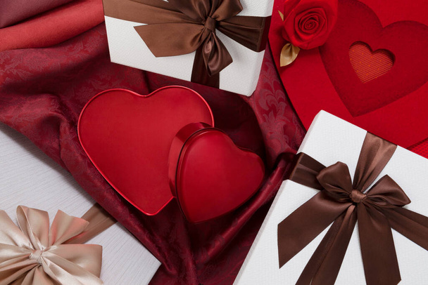 Ystävänpäivä tausta, koostumus lahjapakkauksia ja punainen sydän metallin muotoinen laatikot, jouset ja nauhat, ylhäältä näkymä ruusunpunainen kangas. Hyödyllinen onnittelukortti tai juliste malli - Valokuva, kuva