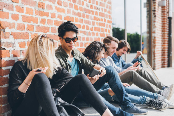 Grupo de amigos multiétnicos millennials usando teléfonos inteligentes adictos a las tendencias tecnológicas siguiendo y charlando  - Foto, imagen