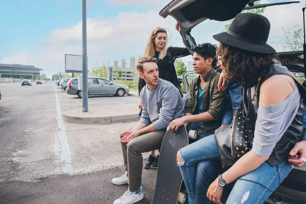 Grupo mixto de amigos de aventura sentados en el maletero del coche charlando y divirtiéndose juntos - Foto, Imagen