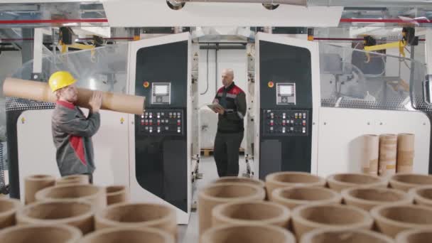 Filmati medi al rallentatore di operai in tuta uniforme che lavorano alla produzione di tubi di cartone a spirale per avvolgere il polietilene - Filmati, video