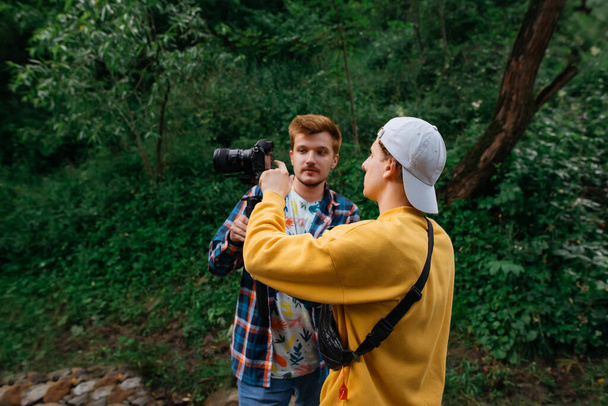 Deux vidéastes masculins créent des vidéos dans la nature, un gars tient une caméra sur un stabilisateur et communique avec un collègue. Des amis filment des vidéos de voyage en vacances lors d'une randonnée. Création de contenu vidéo. - Photo, image