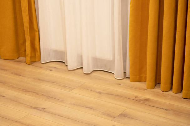 Vista de la parte de la habitación con cortinas naranjas y blancas y suelo de madera - Foto, Imagen