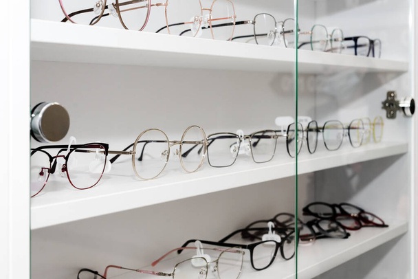 Eyeglasses in optical store, fashion, different glasses on white shelf in shopping mall. Selective focus. - Photo, Image