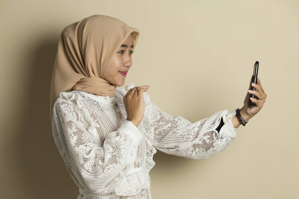 χαρούμενη νεαρή Ασιάτισσα μουσουλμάνα που χρησιμοποιεί κινητό τηλέφωνο - Φωτογραφία, εικόνα
