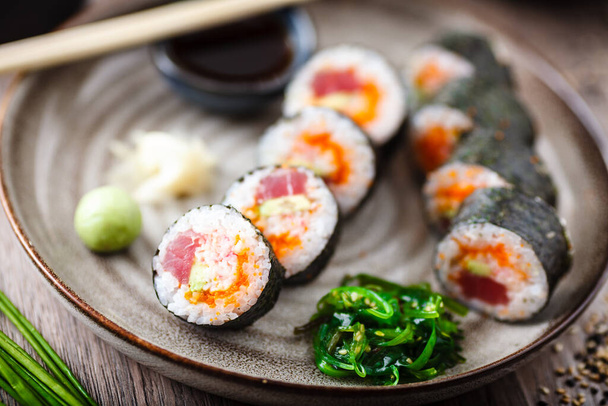 Rollos de maki de sushi con atún, caviar de pescado volador, cangrejo, aguacate en un plato con palillos, salsa de soja, wasabi y jengibre. Primer plano de la comida tradicional japonesa servida para el almuerzo en el restaurante gourmet moderno. - Foto, imagen