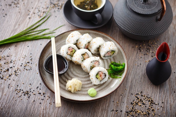 Sushi maki rollos de California con cangrejo, pepino y aguacate en un plato con palillos, salsa de soja, wasabi y jengibre. Marisco tradicional japonés servido para el almuerzo en el restaurante gourmet moderno. - Foto, Imagen