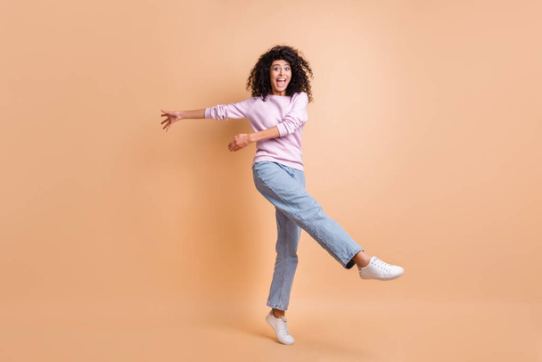 Full size photo of optimistic curly girl dancing wear sweater jeans sneakers isolated on peach color background - Foto, imagen
