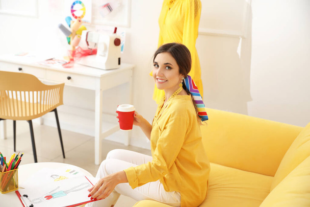 Female fashion designer with cup of coffee working in studio - Zdjęcie, obraz
